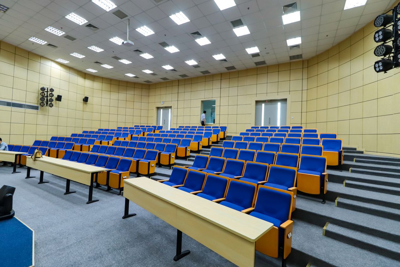 Offerings Spacious lecture hall with blue seats and desks ready for students.